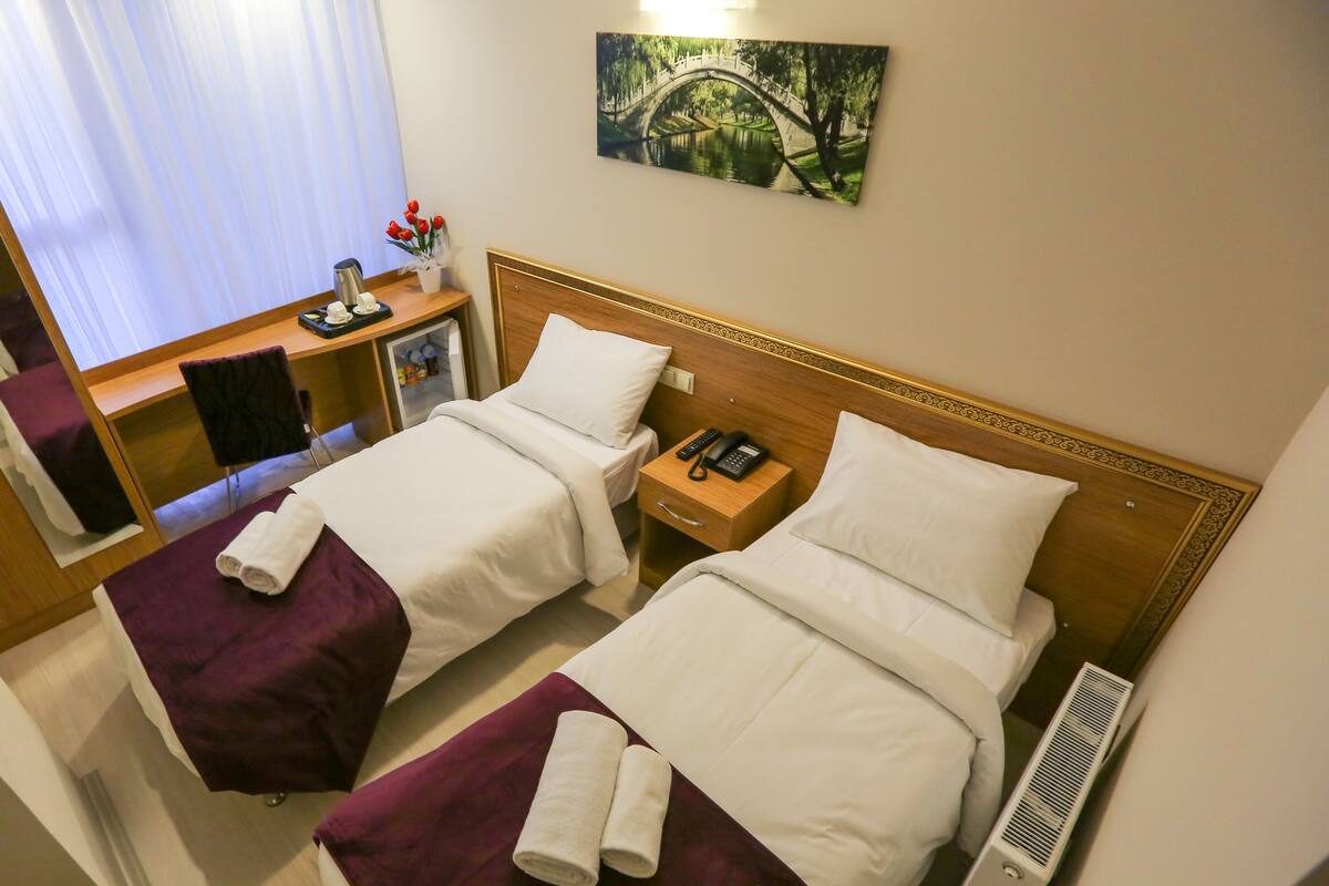 A hotel room with two beds, a desk with a chair, a telephone, and a painting on the wall.