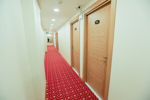 A hotel hallway with red carpet, wooden doors, and a security camera.