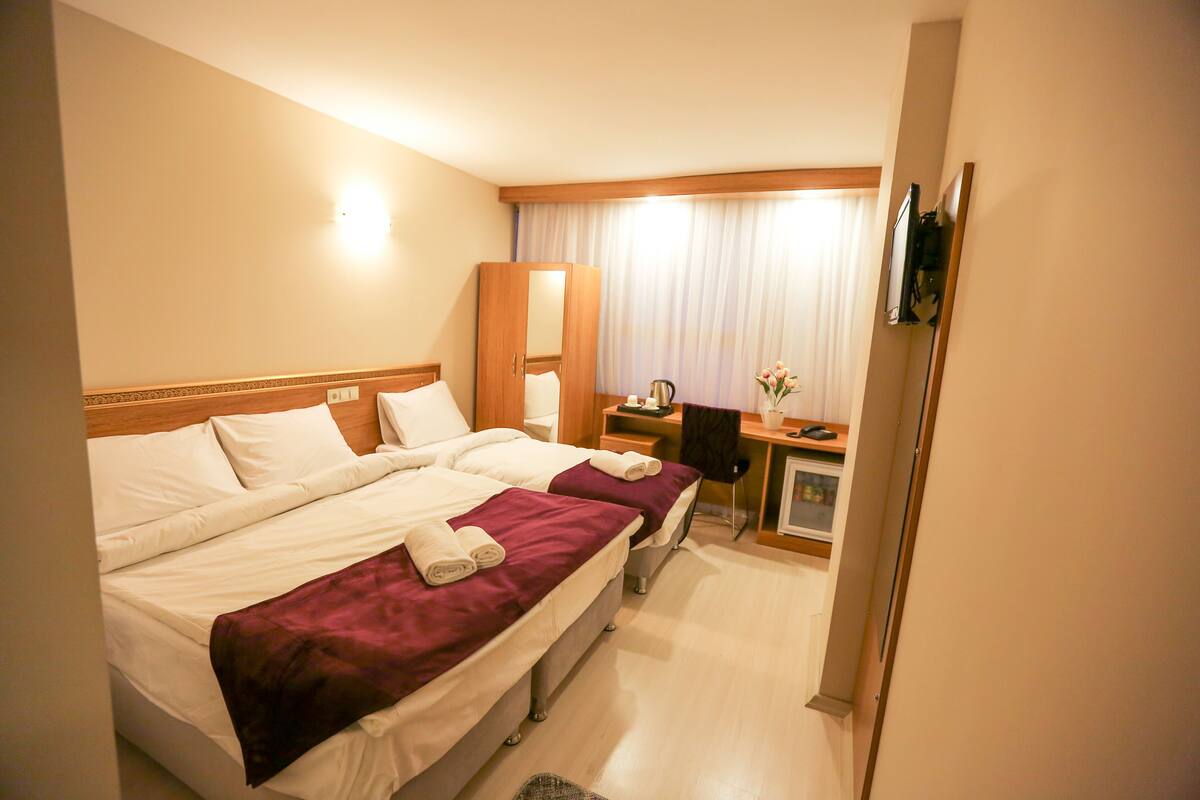A hotel room with two beds, a desk, a chair, a television, and a window with curtains.