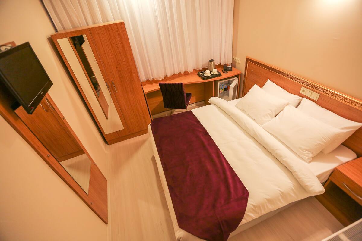 A hotel room with a bed, a desk, a chair, a TV, and a mirror.