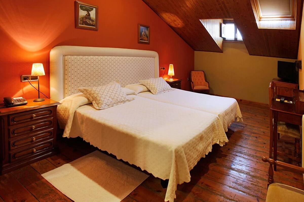 A bedroom with a large bed, two bedside lamps, a wooden dresser, and a small chair.