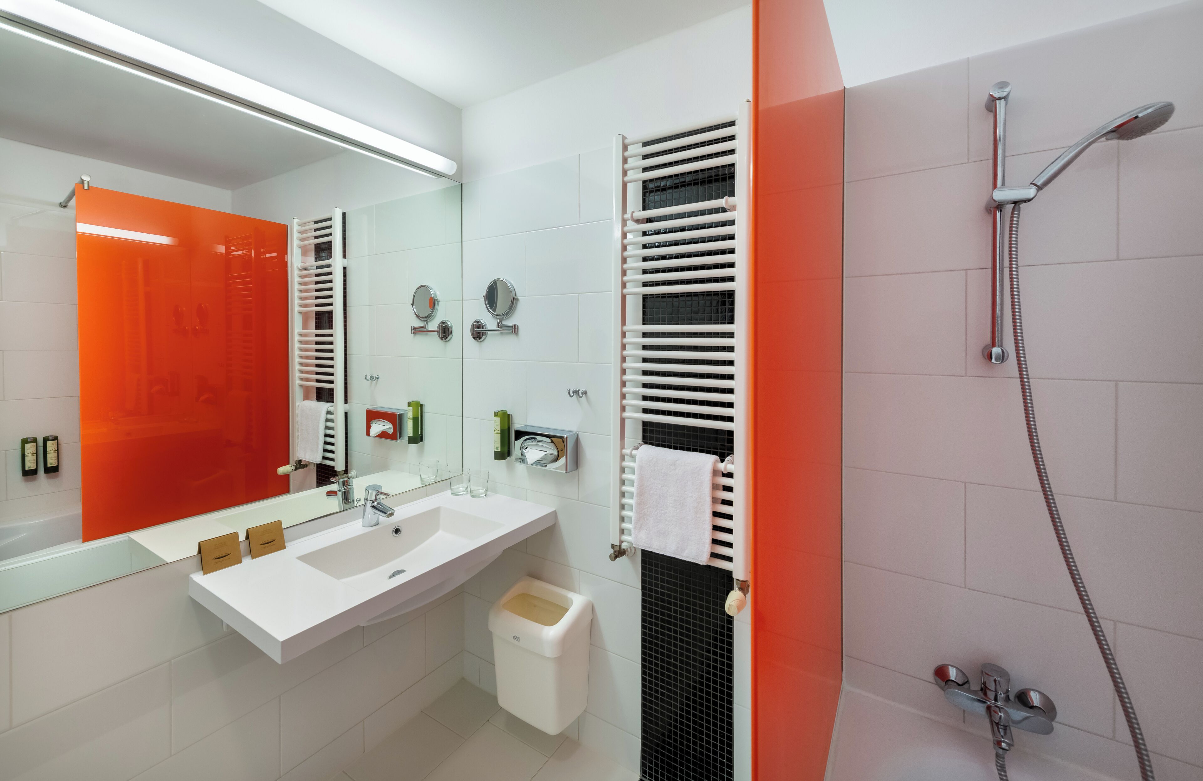 A modern bathroom with a white sink, two mirrors, a towel rack, and a shower with a handheld showerhead.