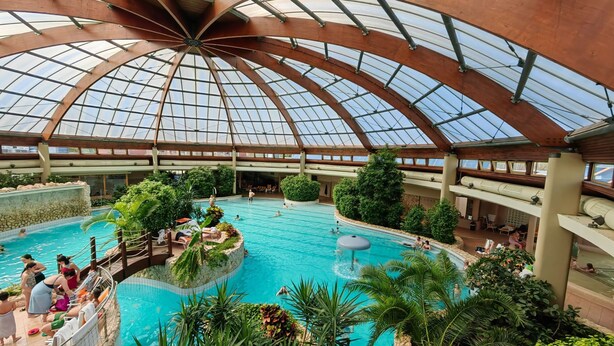 Una piscina interior con techo de vidrio, rodeada de vegetación y varios niveles.