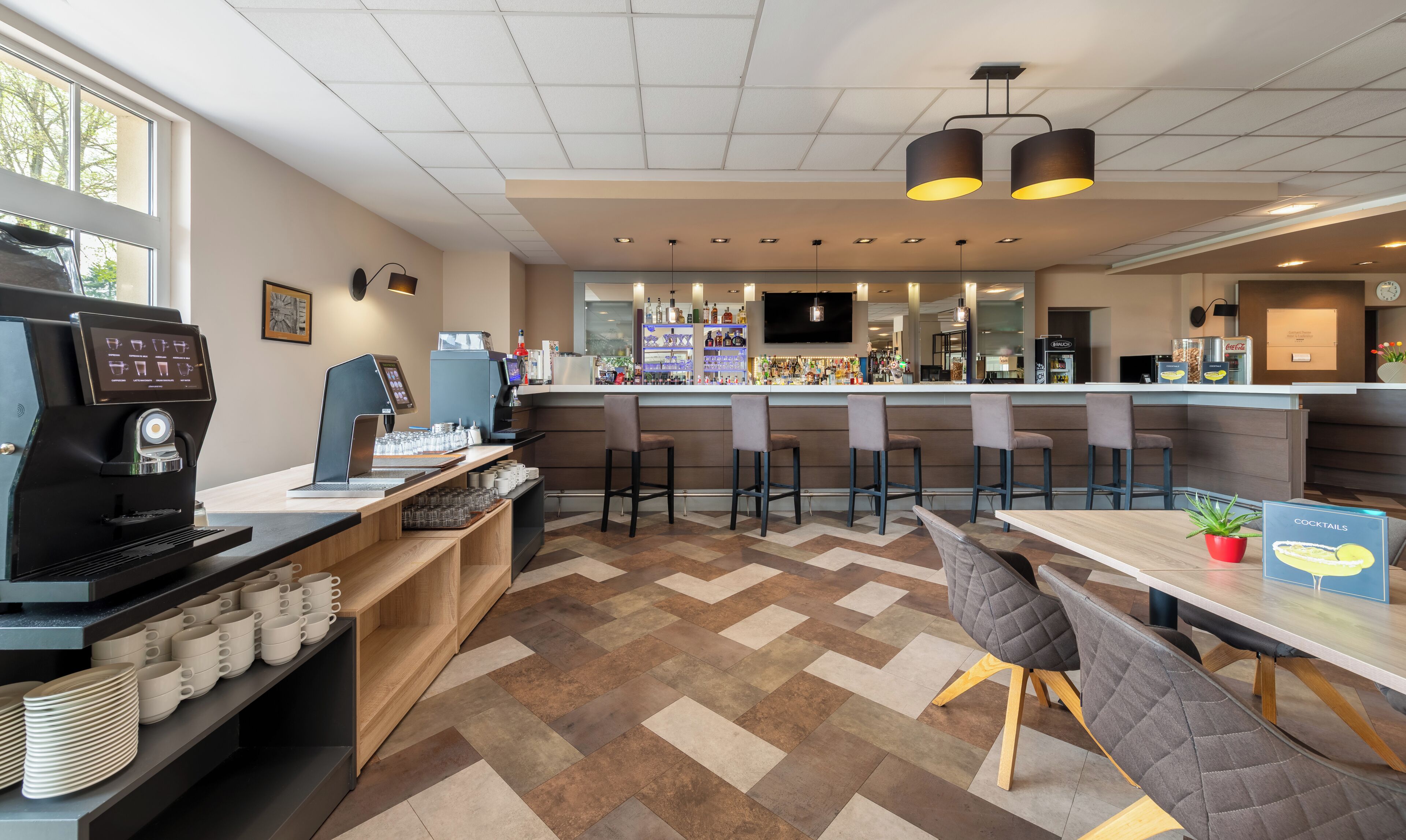 A modern bar area with a coffee machine, seating, and a counter with various bottles.