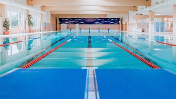 Una piscina interior larga con carriles bien definidos, plantas en macetas y techo de madera.