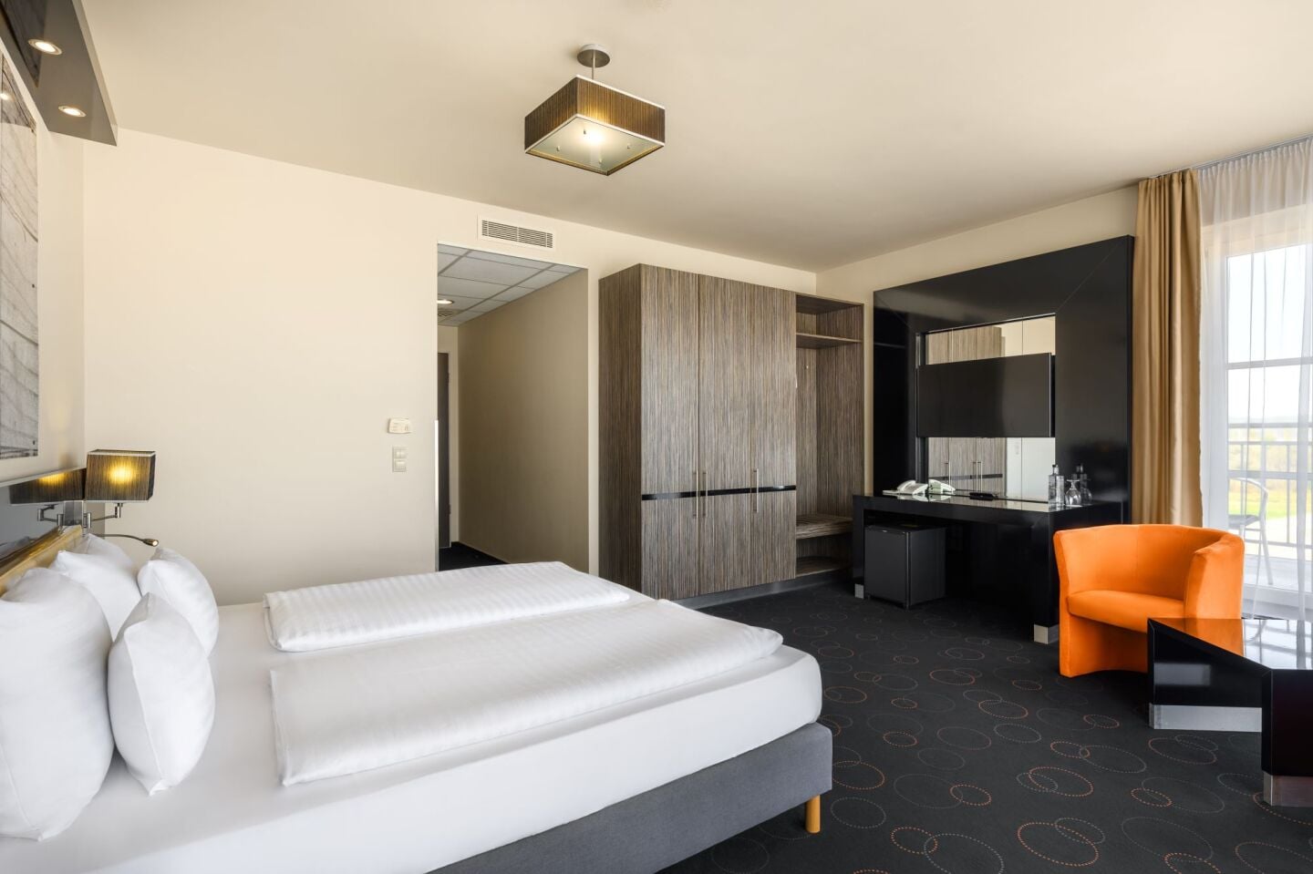 A hotel room with a bed, desk, chair, and a large window.