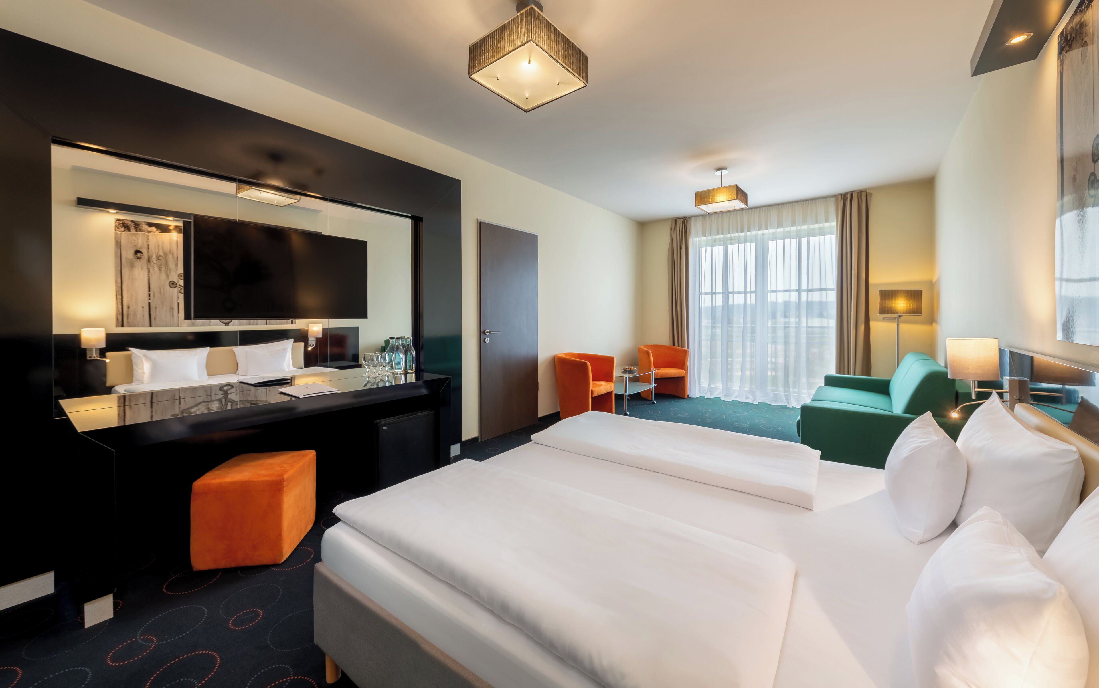 Quarto de hotel com uma cama grande, uma escrivaninha com cadeira, um sofá e uma televisão.