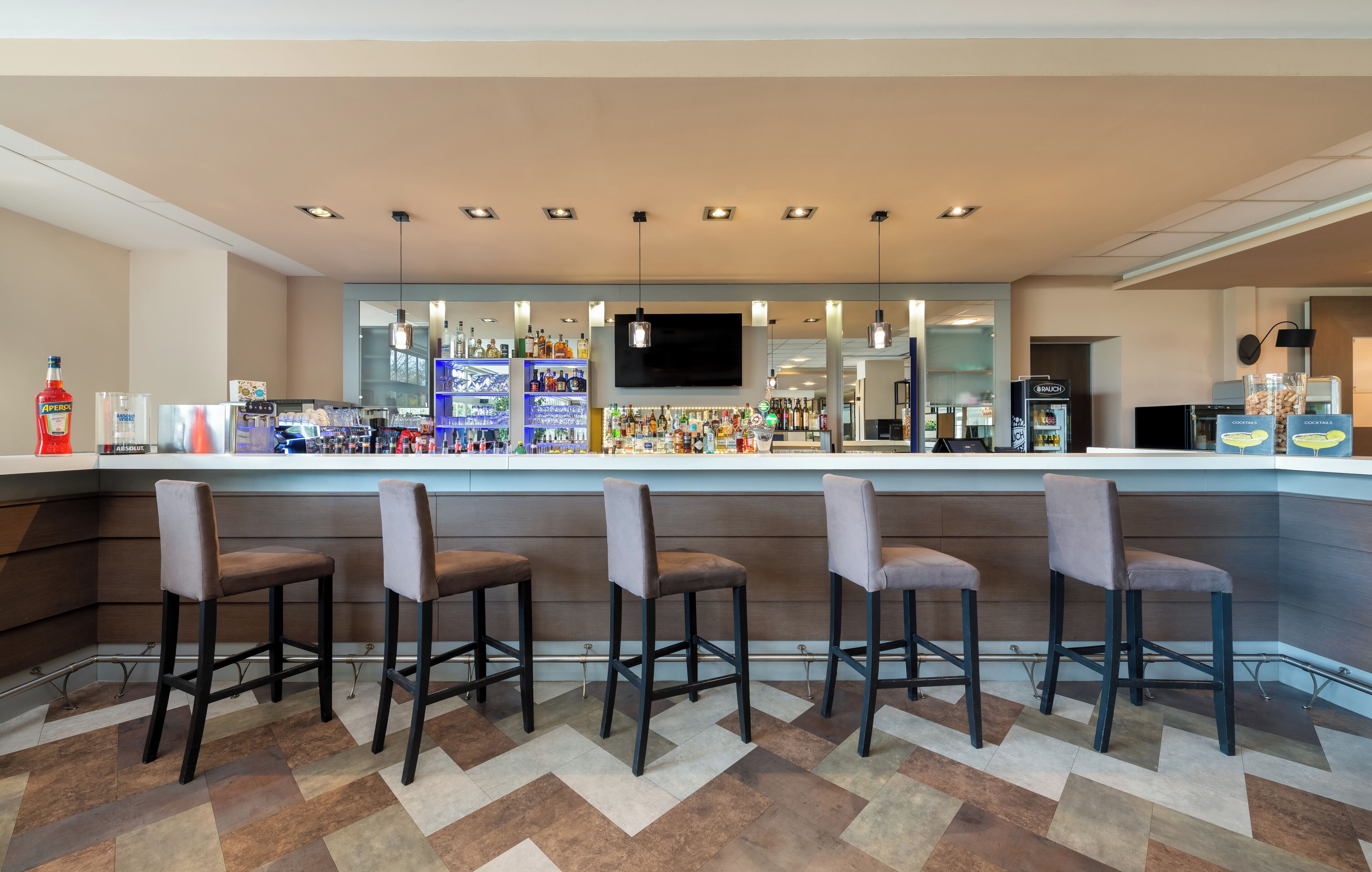A bar area with a counter, bar stools, and a variety of bottles and glasses.