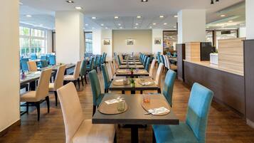 A spacious dining area with multiple tables and chairs, a reception desk, and large windows allowing natural light.