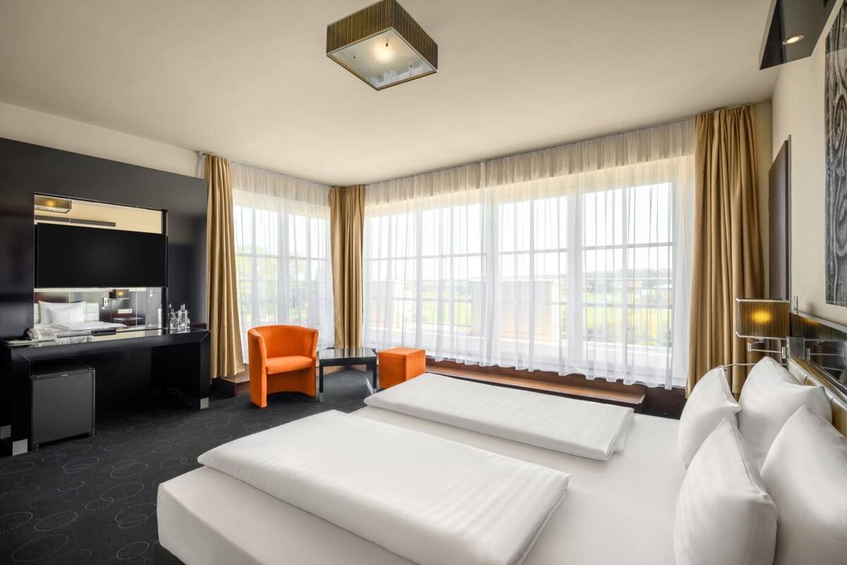 A hotel room with two beds, a desk, a chair, and a TV.