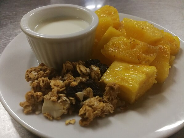 Un plato con un tazón de yogur, trozos de piña y granola.