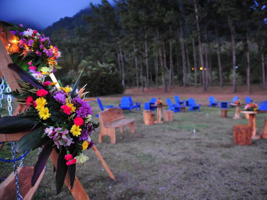 A campsite with wooden benches and tables, surrounded by blue chairs and a forested area in the background.