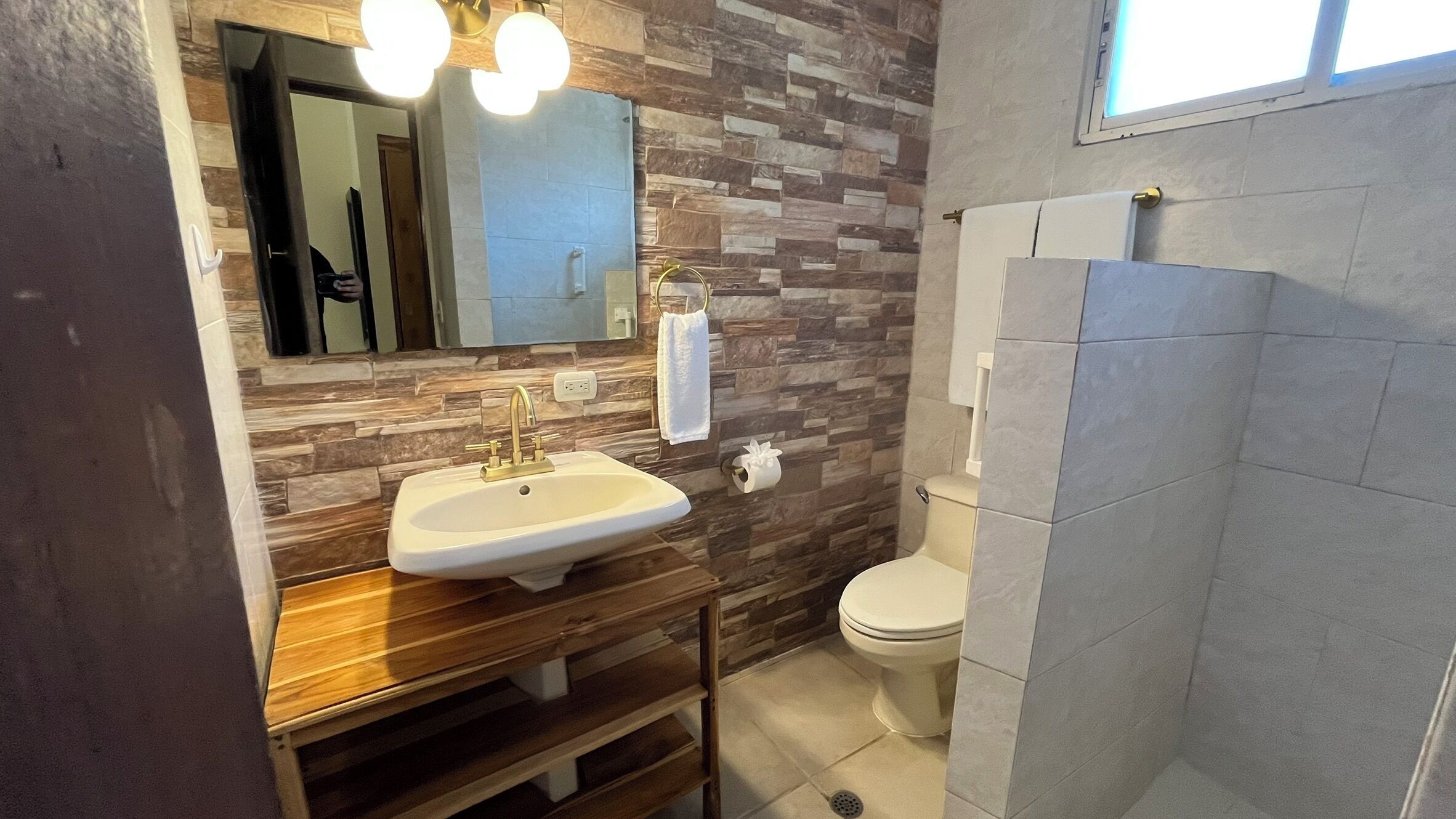A bathroom with a wooden vanity, a sink, a toilet, and a shower area.