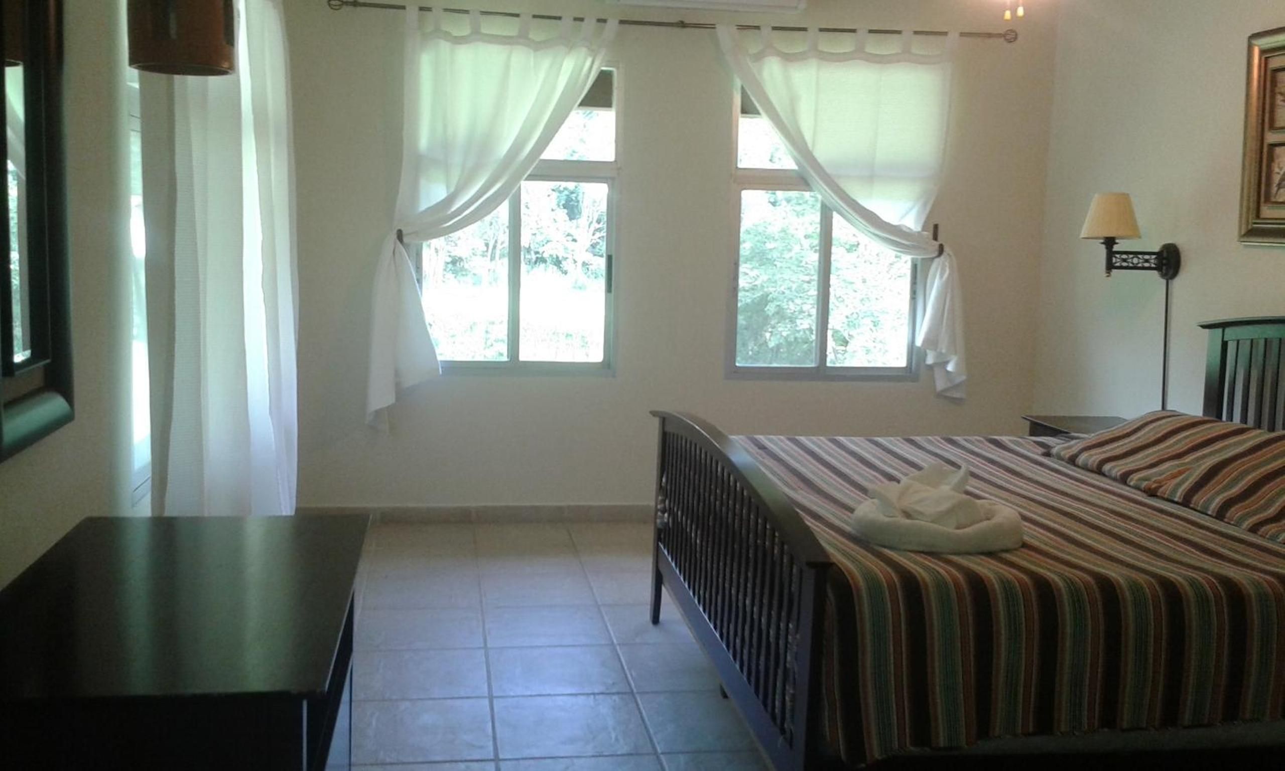 A bedroom with a bed, a nightstand, a lamp, and a window with curtains.