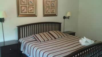 Een netjes opgemaakt bed met een gestreept dekbed en kussens, twee ingelijste kunstwerken met vogelafbeeldingen, en een bedlampje aan beide zijden van het bed.