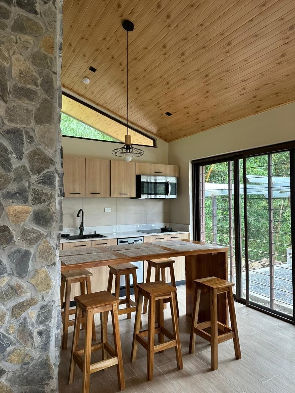 Una cocina moderna con pared de piedra, techo de madera y ventanas grandes.