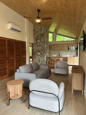 A modern living room with a stone accent wall, wooden ceiling, and a kitchen area with a stone backsplash. - Hotel Campestre (El Valle de Anton)