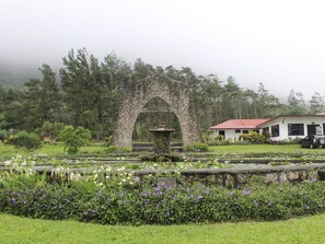 A garden with a stone archway, a pond with water lilies, and a building with a red roof. - Hotel Campestre (El Valle de Anton)