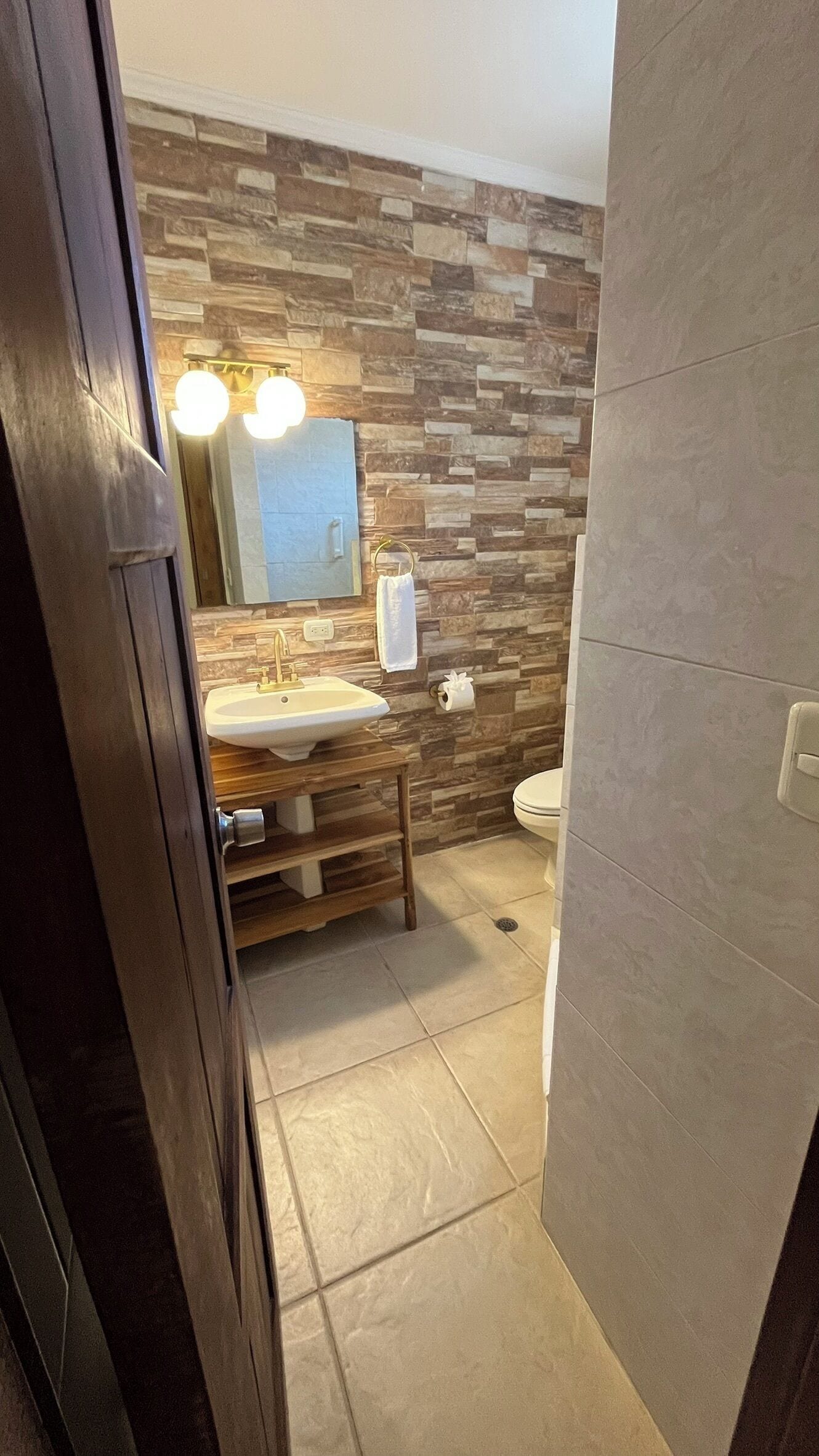 A bathroom with a stone wall, a sink, a toilet, and a mirror.
