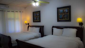 Two single beds with wooden headboards, a ceiling fan, and framed pictures on the walls.