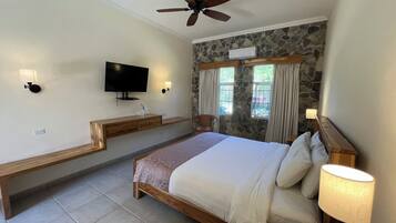 A bedroom with a bed, a television, a stone wall, and a window with curtains.