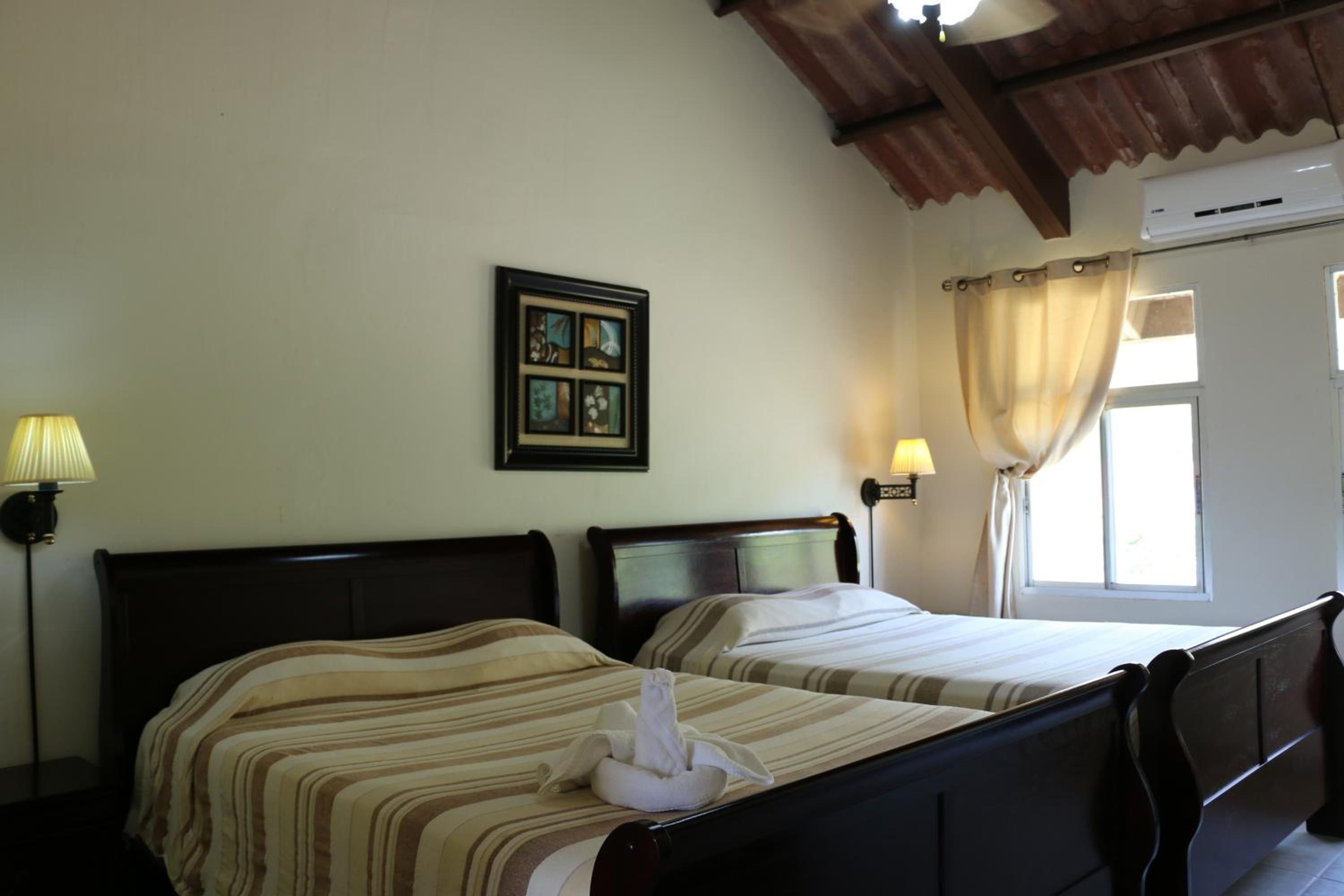 A hotel room with two beds, a framed picture on the wall, and a window with curtains.