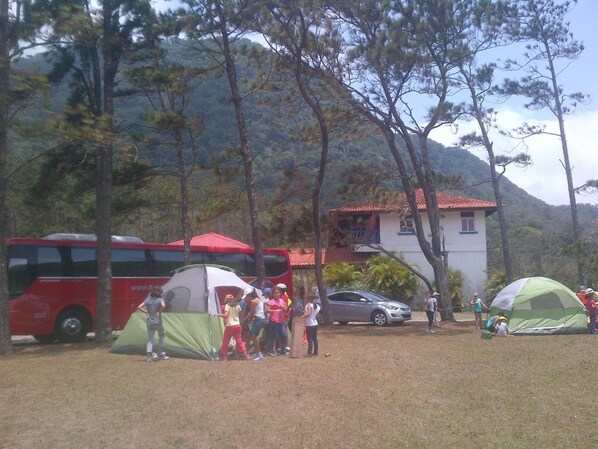 A campsite with tents, a bus, and a building in a wooded area. - Hotel Campestre (El Valle de Anton)
