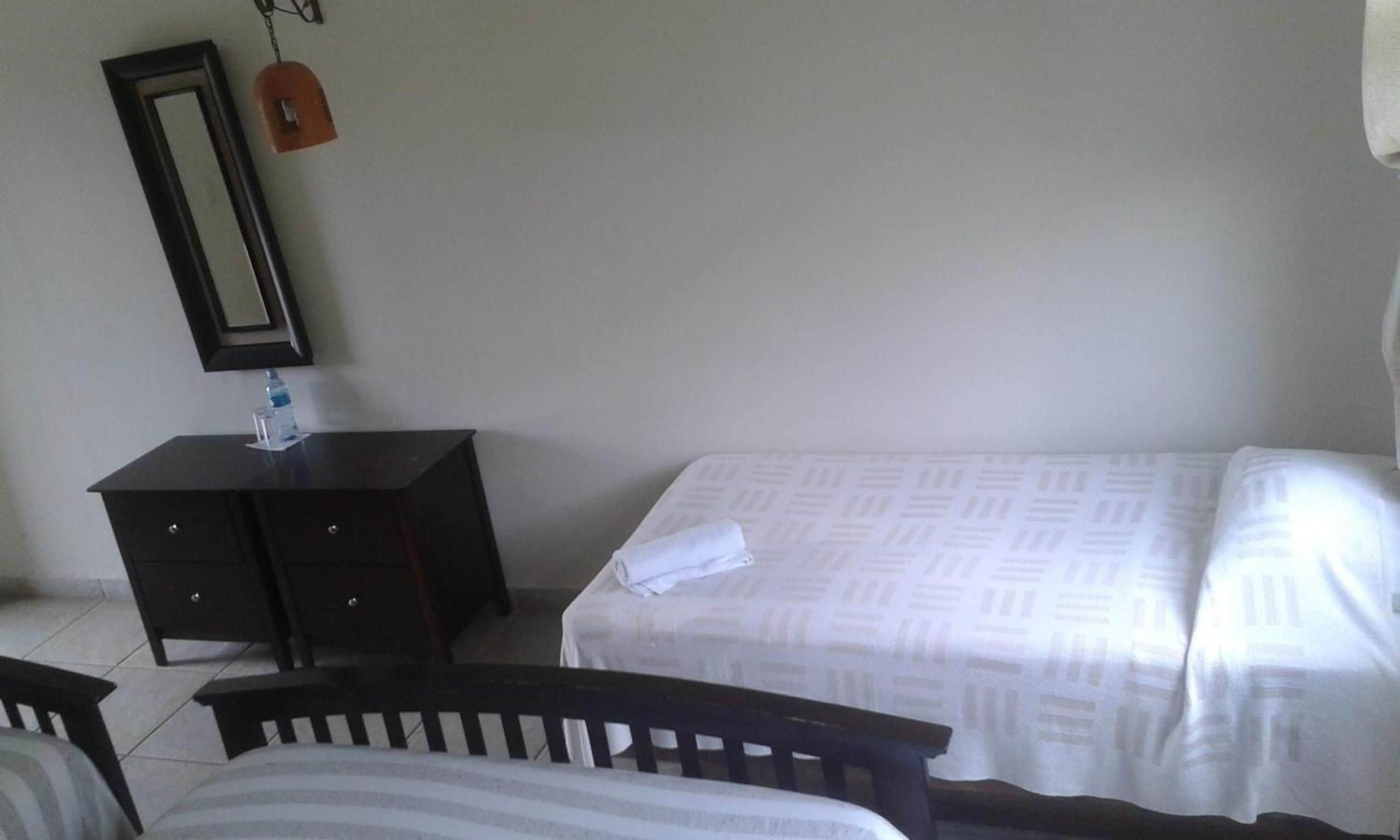 A hotel room with a bed, a small bedside table, a mirror, and a wardrobe.
