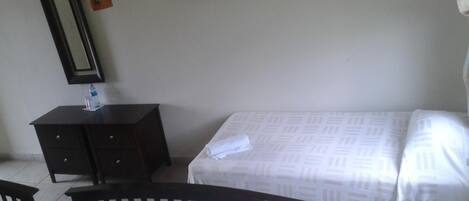A hotel room with a bed, a small bedside table, a mirror, and a wardrobe.