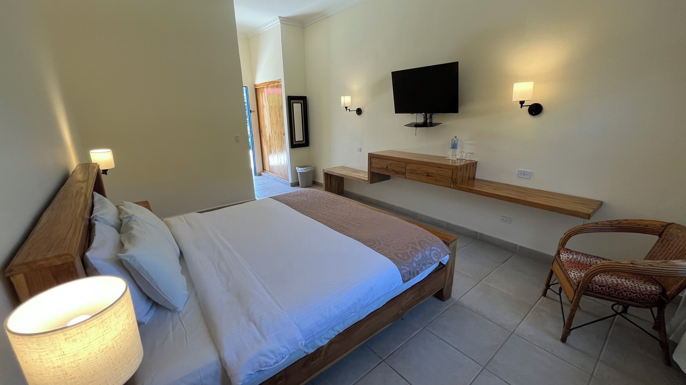 A bedroom with a bed, bedside lamps, a TV, a bench, and a chair.