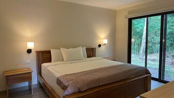 A bedroom with a bed, bedside tables, a ceiling fan, and a large window with a view of greenery.
