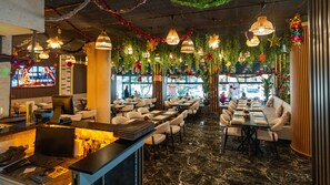 A restaurant interior with multiple dining tables and chairs, hanging decorative lights, and a bar area with a laptop and mouse. - Hotel Diana (Istanbul)