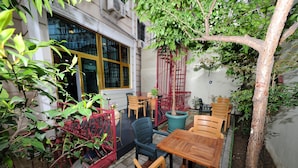 Un patio con mesas y sillas de madera, una valla metálica roja y un árbol.