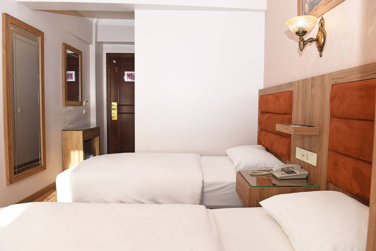 Une chambre d’hôtel avec deux lits, une tête de lit en bois, une table de chevet avec une lampe et un miroir au mur.