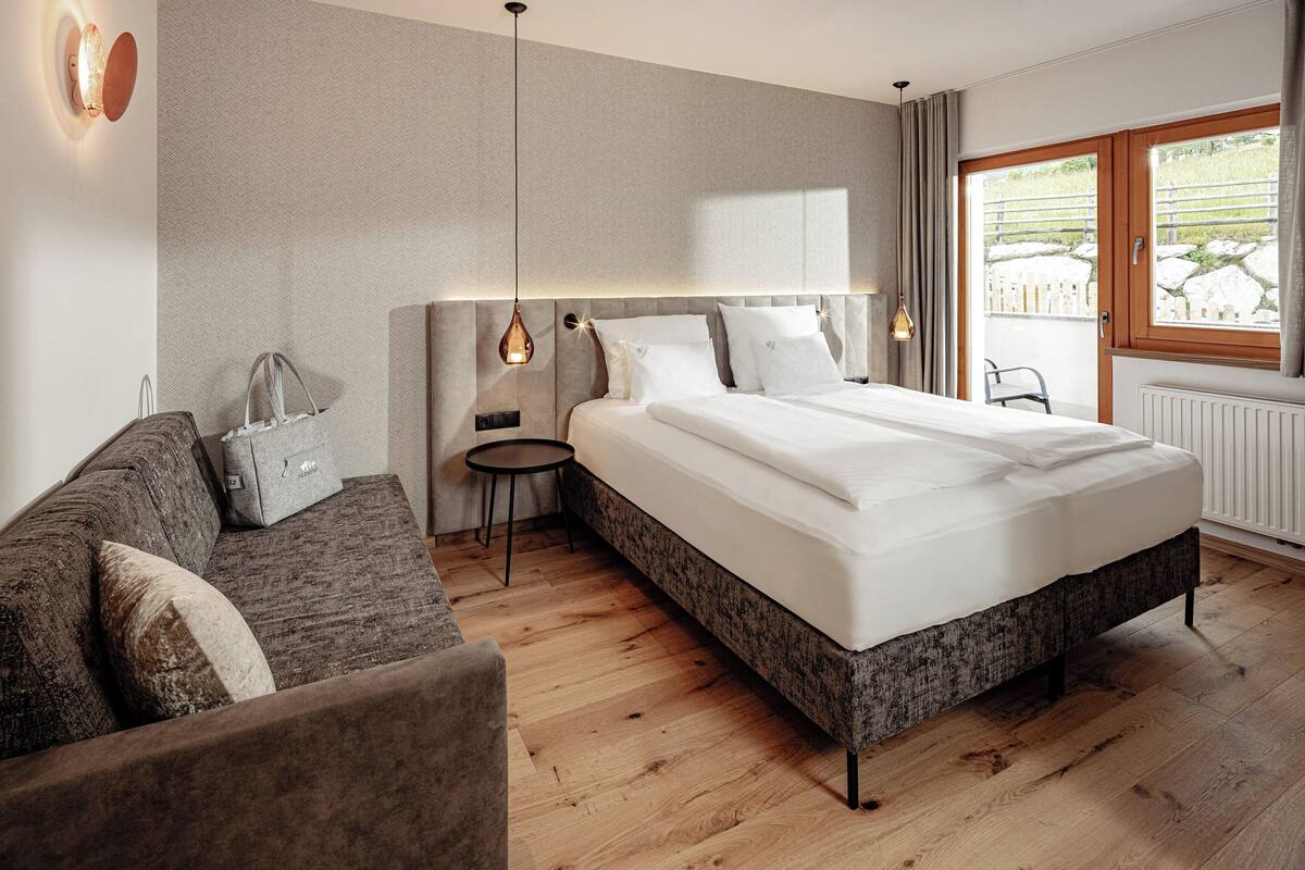 Une chambre d’hôtel moderne, dotée d’un grand lit, d’un canapé, d’une petite table d’appoint et offrant une vue sur l’extérieur grâce à une grande fenêtre.