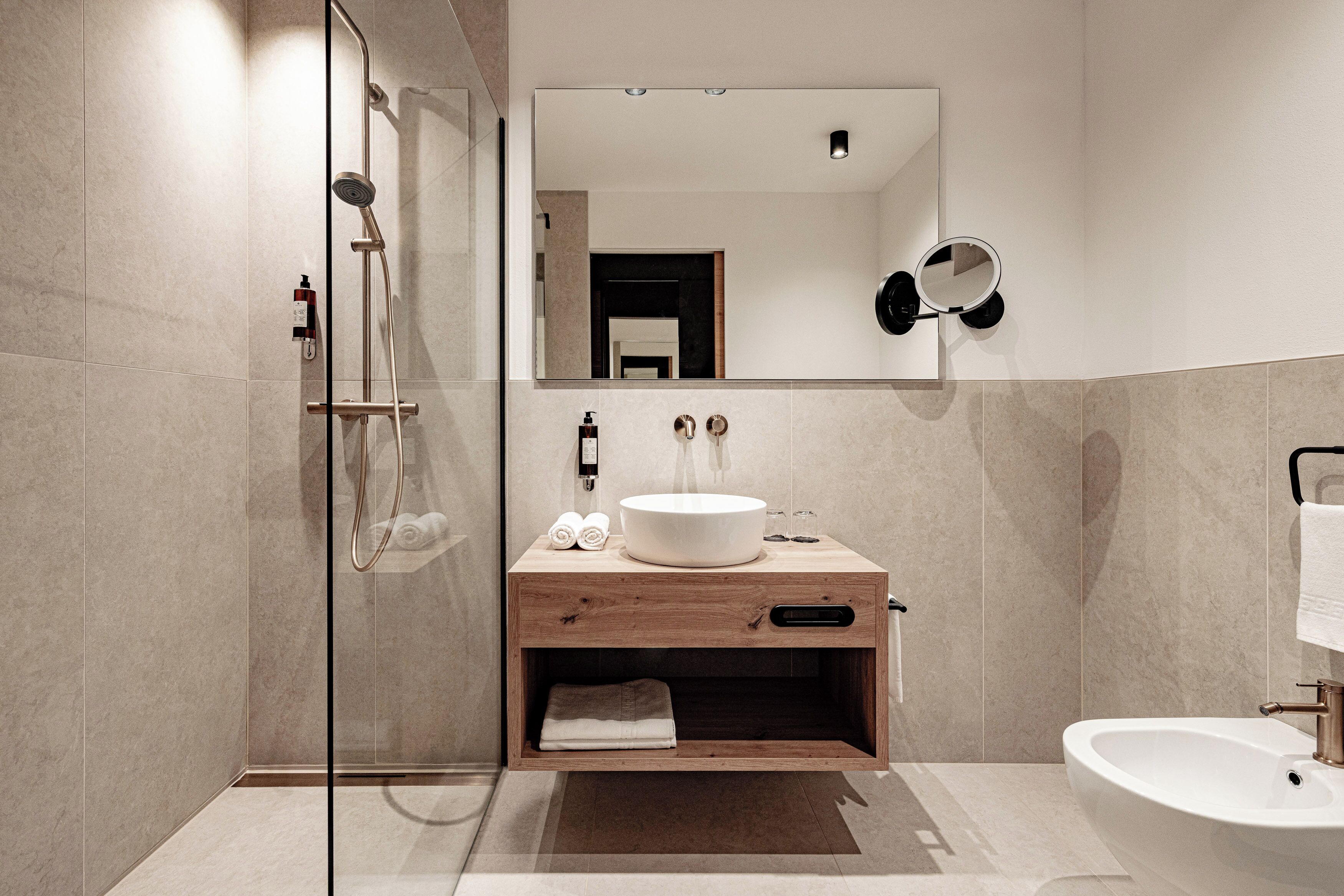 Un baño moderno con ducha envuelta en vidrio, tocador de madera con lavamanos y bañera independiente.