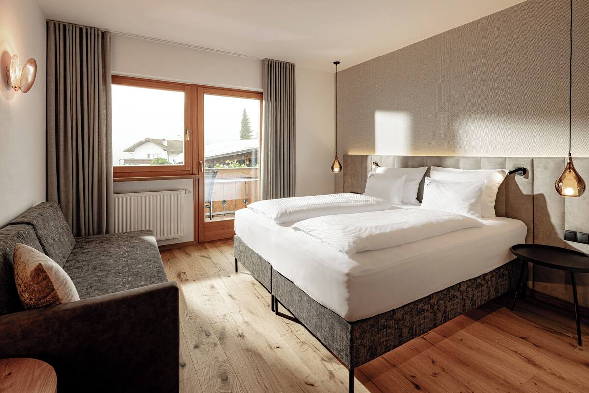 Une chambre d’hôtel moderne dotée d’un grand lit, d’un canapé, d’une petite table et offrant une vue sur l’extérieur grâce à une porte coulissante.