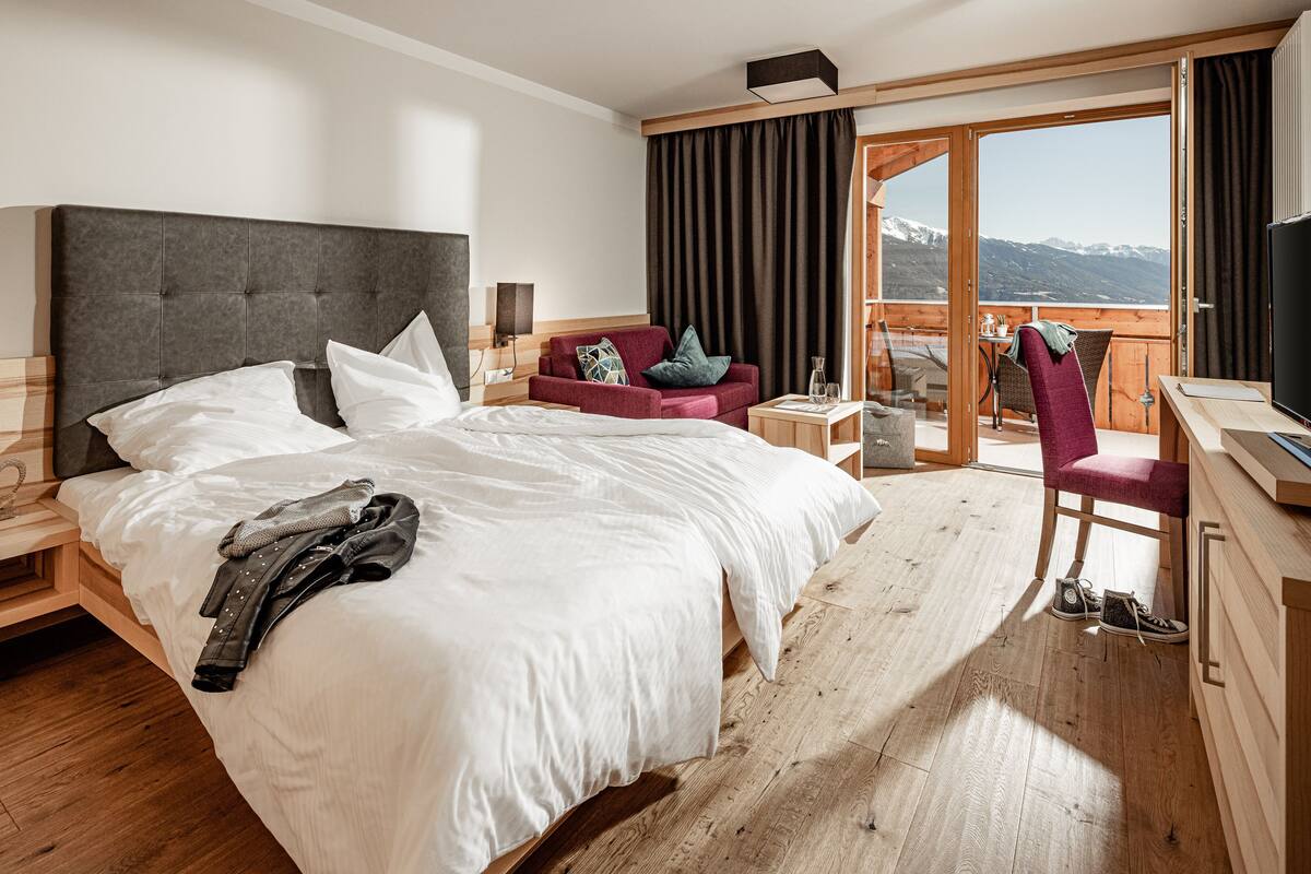 Une chambre d’hôtel dotée d’un grand lit, d’un bureau, d’une chaise, d’un canapé et d’un balcon offrant une vue sur les montagnes.