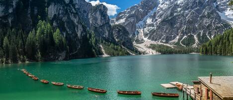 A wooden dock with several boats lined up on a turquoise lake, surrounded by forested mountains.