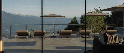 A terrace with outdoor seating and umbrellas, overlooking a mountainous landscape.