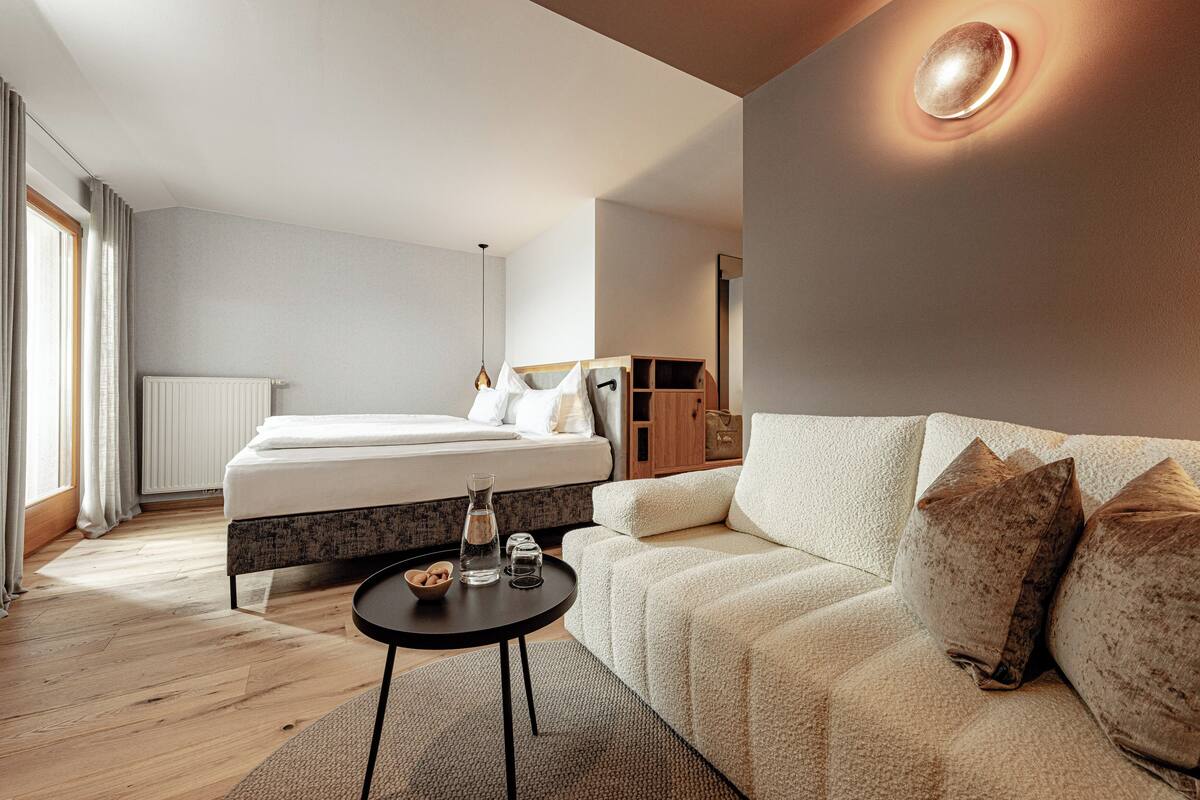 Une chambre à coucher moderne avec un lit, un canapé, une petite table et une lampe de chevet.