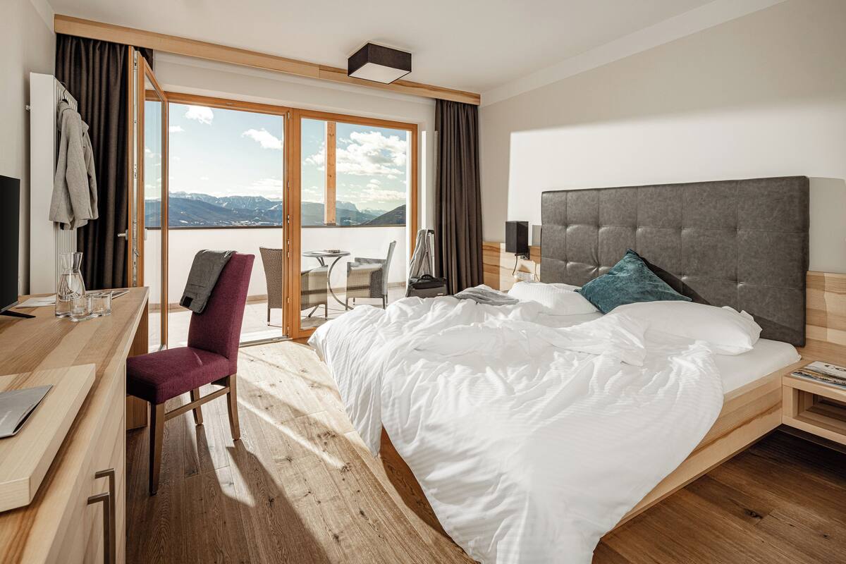 Une chambre d’hôtel moderne avec un grand lit, un bureau, une chaise et une vue sur les montagnes.