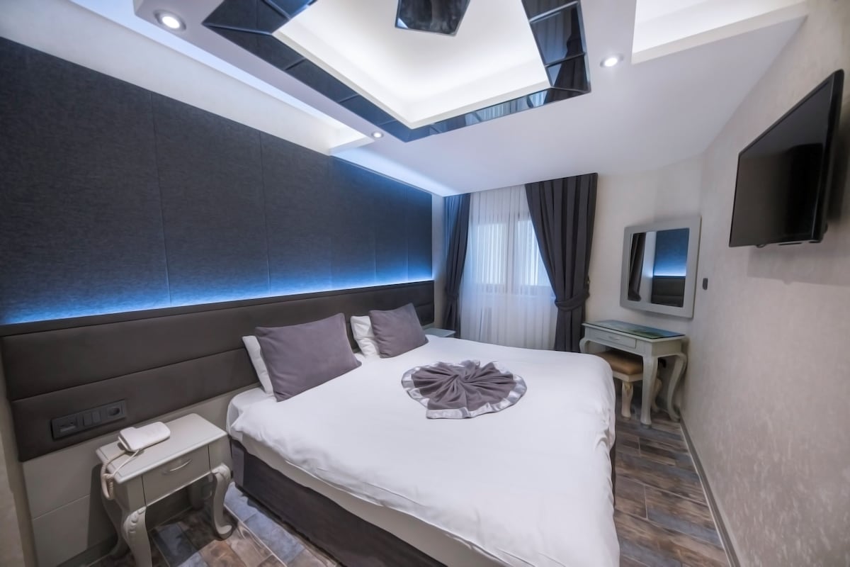 A hotel room with a bed, bedside table, phone, and a desk with a chair.