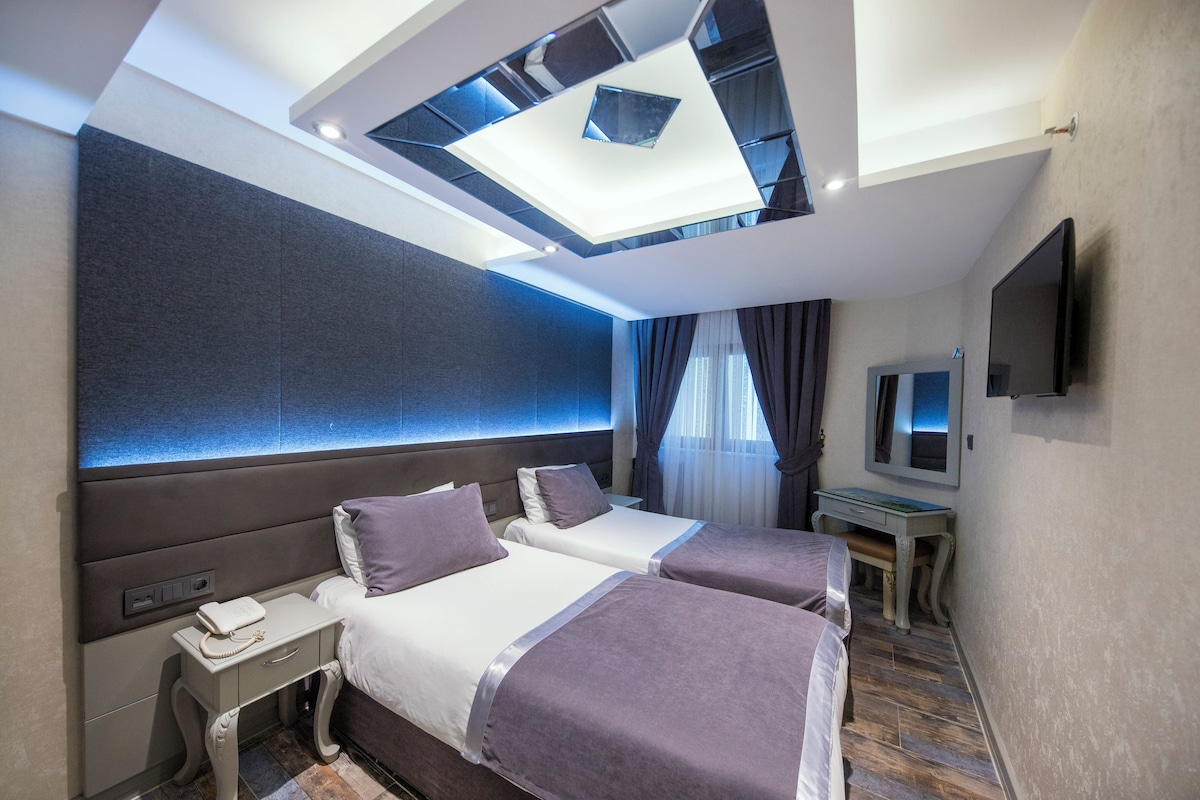 A modern hotel room with two beds, a desk, a flat-screen TV, and a skylight.