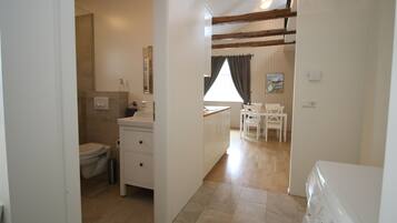A bathroom with a toilet, sink, and mirror. There is a window with curtains and a painting on the wall.