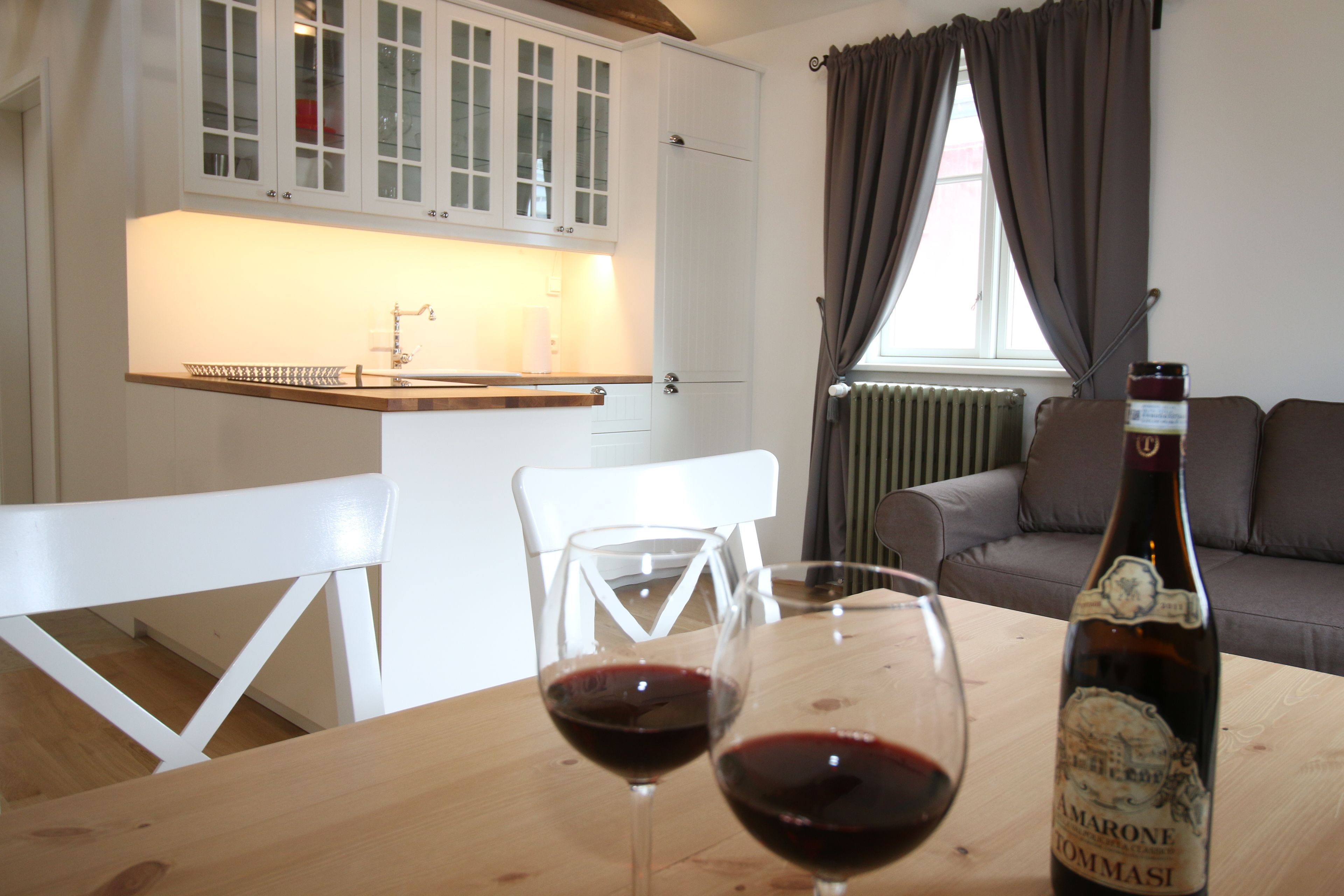 A dining area with a wooden table, two wine glasses, and a bottle of Amarone Romasi wine.