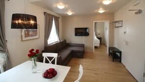 Una sala de estar moderna con un sofá blanco, una mesa de comedor con un jarrón de rosas rojas y un televisor de pantalla plana montado en la pared.