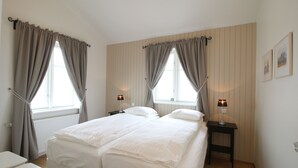 Una cama doble con dos mesitas de noche, un tocador blanco y una ventana con cortinas.