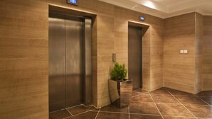 A modern elevator area with two elevators, a digital display, and a potted plant. - L'eola Suites (Abuja)