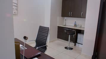 A small office with a desk, a chair, a kitchenette, and a refrigerator.